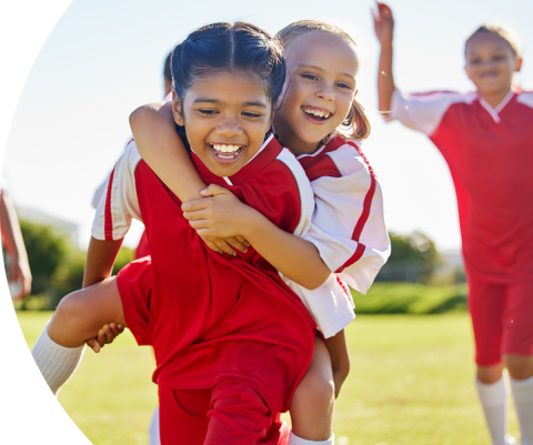 Duas meninas em uniformes esportivos sorrindo e se abraçando ao ar livre