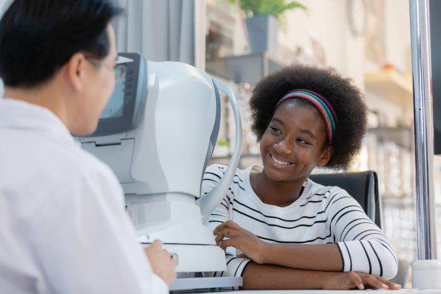 Profissional de saúde ocular ao lado de uma menina sorridente durante um exame